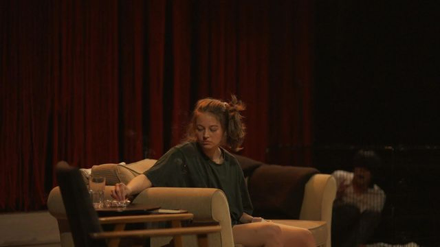 Kvinne i sofa slukker røyk i askebeger på bord ved sofa. Bilde fra forestilling