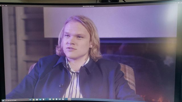 Bilde fra skjerm av mann i stol som blir intervjuet