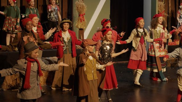 Barn i kostymer danser på scene. Bilde fra forestilling